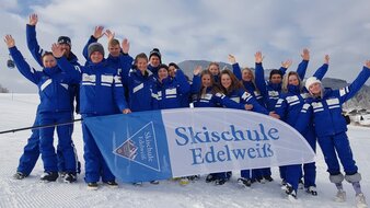 Skischule Edelweiß Skilehrer Gruppenfoto im Schnee mit Skischul-Fahne | © Skischule Edelweiß
